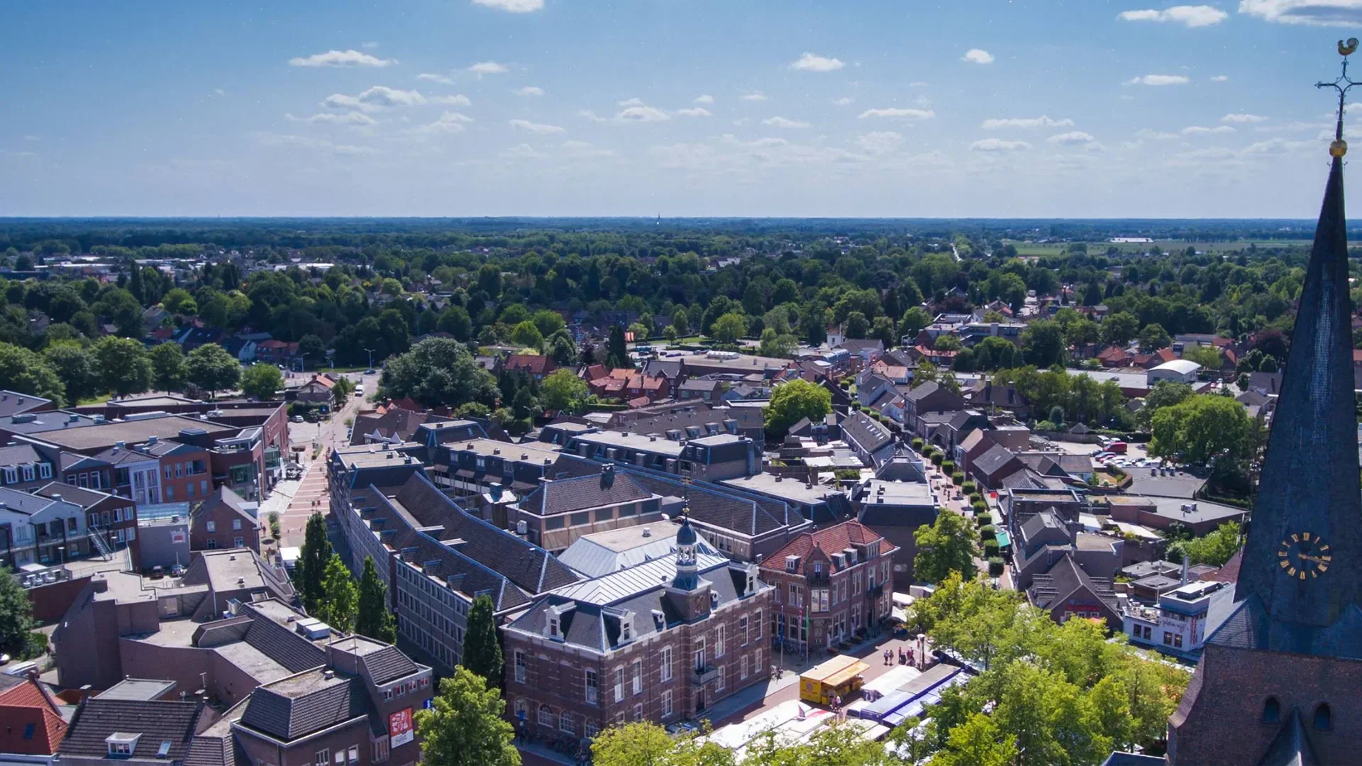 Luchtfoto van het centrum van Deurne met het oude gemeentehuis, de markt en de kerktoren, met daarachter het groene buitengebied