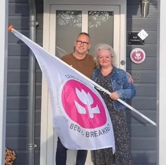 De eigenaren van B&B Sterrenhemel bij de voordeur van het chalet met de vlag van Certified Bed & Breakfast