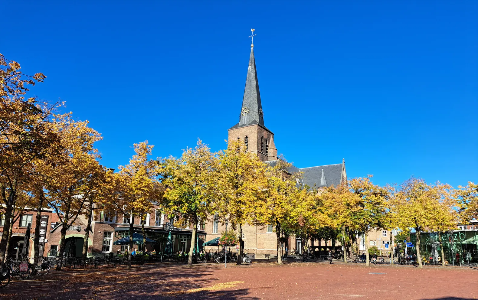 De Markt in Deurne met de Sint-Willibrorduskerk, terrassen en herfstbomen