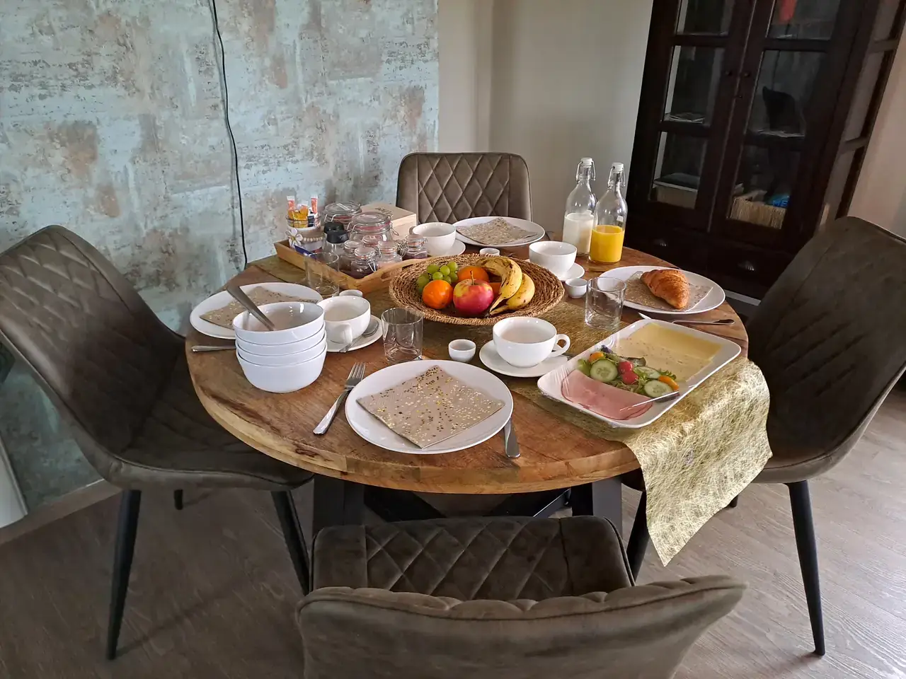 Gedekte ronde ontbijttafel met fruitschaal, croissant, kaas, ham, salade en potjes met beleg