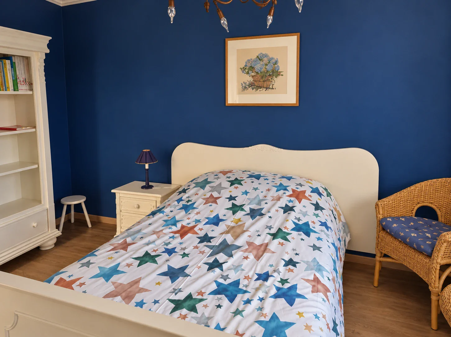 Tweede slaapkamer met blauwe wand, twijfelaar met sterrendekbed, nachtkastje, boekenkast en rieten stoel