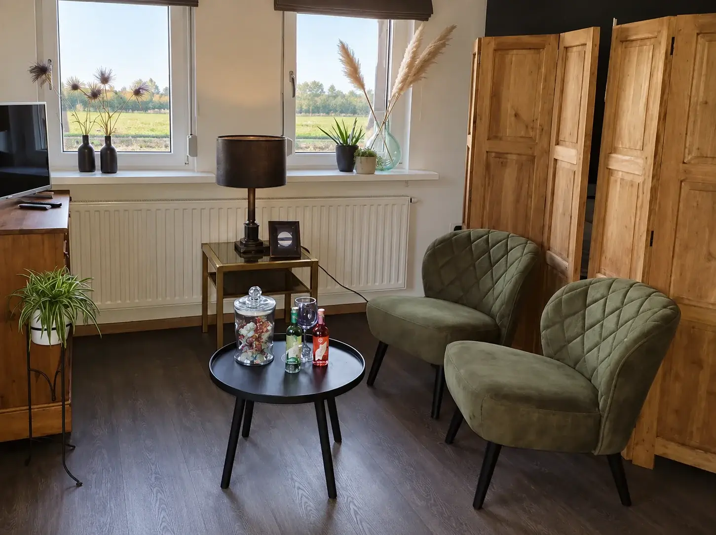 Zithoek met twee groene fauteuils, een bijzettafel met welkomstdrankje en uitzicht op de weilanden